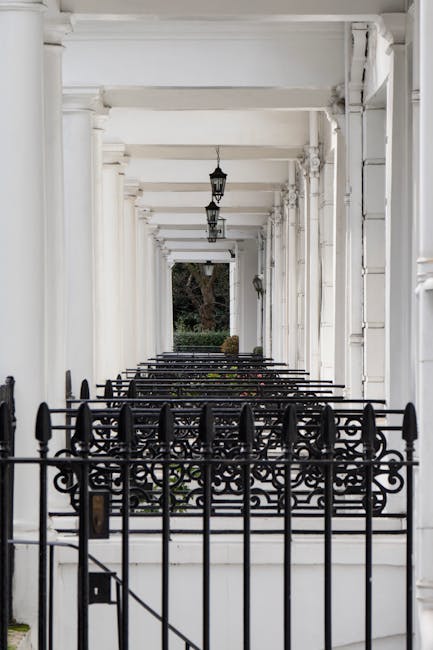 A row of colorful, terraced houses in Kensington with pastel facades painted in shades of light blue, yellow, and lavender, each featuring white-framed windows and small front steps leading to black i